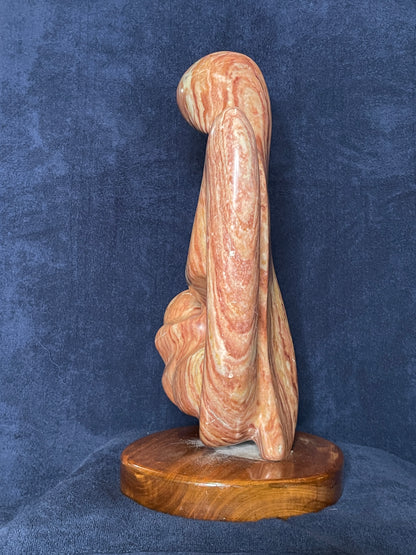 Cherish is carved from Utah red alabaster. Its smooth surface conveys a sense of tranquility and grace. represents the eternal bond of love between a mother and child. This is the first time a human being experiences love through the gentle touch of his/her mother. That is an everlasting love for both of them.

This sculpture was designed and carved by Shahla Rahimi Reynolds.

This piece is: 10" Width x 17 1/2" Height x 6 1/2" Depth.