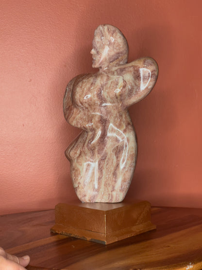 A hand-carved Utah alabaster sculpture depicting Venustus (pronounced veh-NUSS-tuss), the Goddess of Love, showcasing an elegant and refined female form. It represents the qualities of beauty, confidence, and self-assurance, embodying a woman who confidently navigates her own journey through life. The sculpture reflects themes of independence and personal strength, celebrating resilience and empowerment.

Venustus is an original design created by Shahla Rahimi Reynolds.

The piece is 13" H x 8" W x 3.5" D.