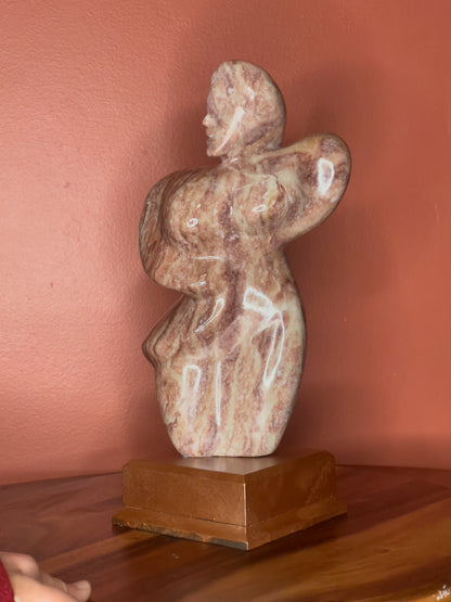 A hand-carved Utah alabaster sculpture depicting Venustus (pronounced veh-NUSS-tuss), the Goddess of Love, showcasing an elegant and refined female form. It represents the qualities of beauty, confidence, and self-assurance, embodying a woman who confidently navigates her own journey through life. The sculpture reflects themes of independence and personal strength, celebrating resilience and empowerment.

Venustus is an original design created by Shahla Rahimi Reynolds.

The piece is 13" H x 8" W x 3.5" D.