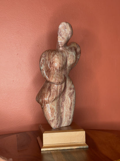 A hand-carved Utah alabaster sculpture depicting Venustus (pronounced veh-NUSS-tuss), the Goddess of Love, showcasing an elegant and refined female form. It represents the qualities of beauty, confidence, and self-assurance, embodying a woman who confidently navigates her own journey through life. The sculpture reflects themes of independence and personal strength, celebrating resilience and empowerment.

Venustus is an original design created by Shahla Rahimi Reynolds.

The piece is 13" H x 8" W x 3.5" D.