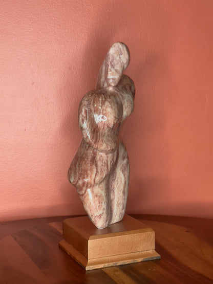 A hand-carved Utah alabaster sculpture depicting Venustus (pronounced veh-NUSS-tuss), the Goddess of Love, showcasing an elegant and refined female form. It represents the qualities of beauty, confidence, and self-assurance, embodying a woman who confidently navigates her own journey through life. The sculpture reflects themes of independence and personal strength, celebrating resilience and empowerment.

Venustus is an original design created by Shahla Rahimi Reynolds.

The piece is 13" H x 8" W x 3.5" D.