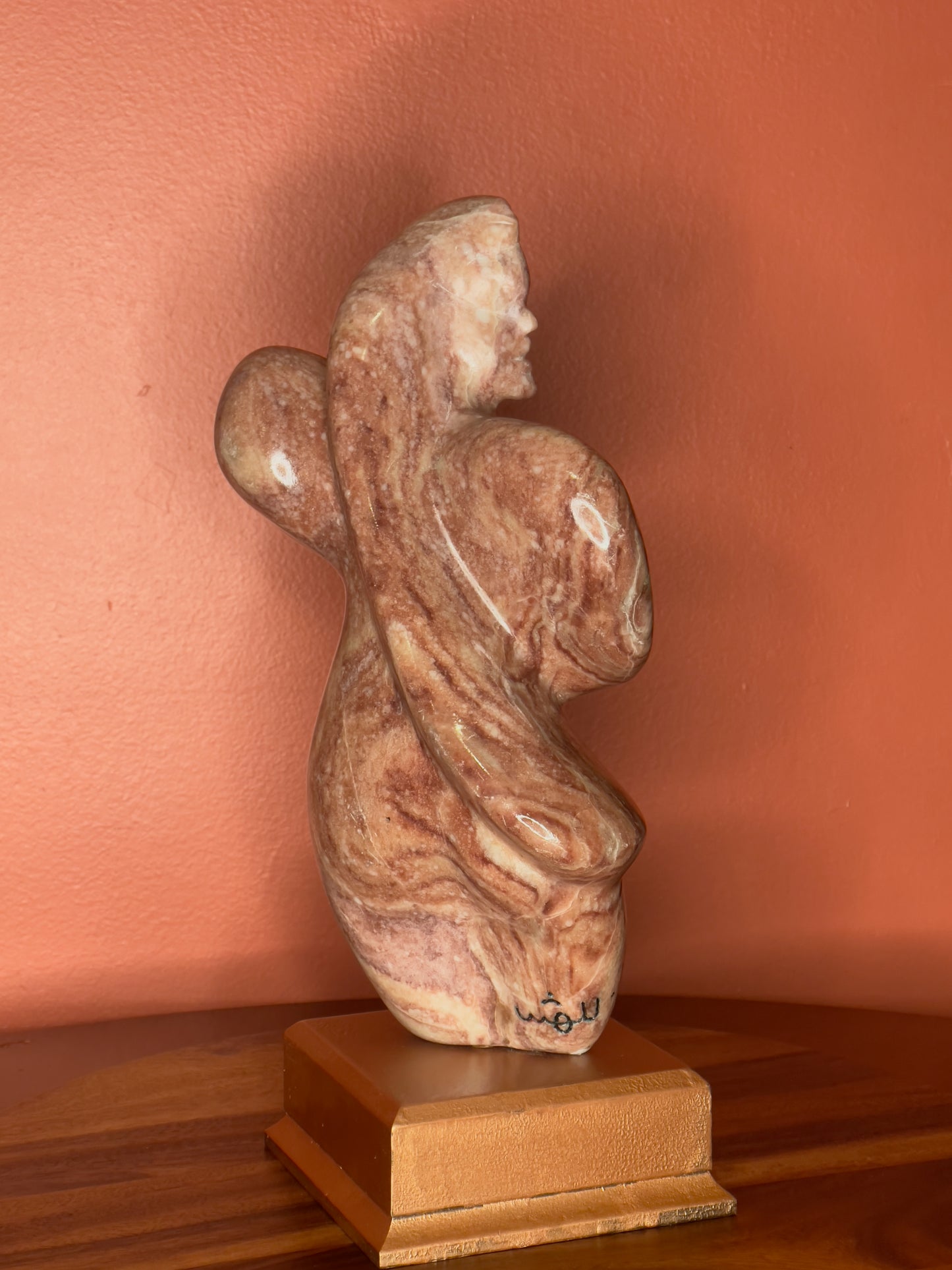 A hand-carved Utah alabaster sculpture depicting Venustus (pronounced veh-NUSS-tuss), the Goddess of Love, showcasing an elegant and refined female form. It represents the qualities of beauty, confidence, and self-assurance, embodying a woman who confidently navigates her own journey through life. The sculpture reflects themes of independence and personal strength, celebrating resilience and empowerment.

Venustus is an original design created by Shahla Rahimi Reynolds.

The piece is 13" H x 8" W x 3.5" D.