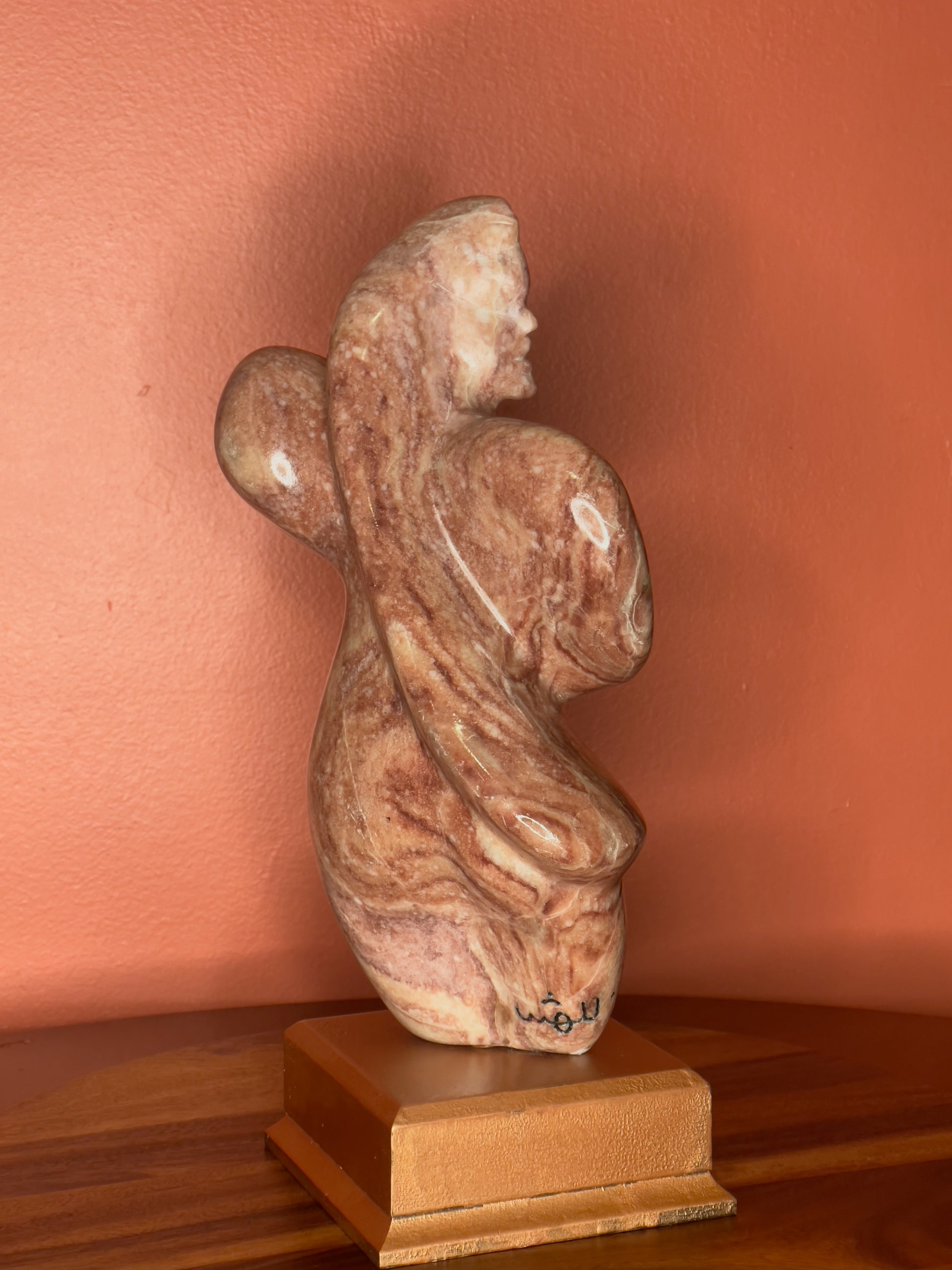 A hand-carved Utah alabaster sculpture depicting Venustus (pronounced veh-NUSS-tuss), the Goddess of Love, showcasing an elegant and refined female form. It represents the qualities of beauty, confidence, and self-assurance, embodying a woman who confidently navigates her own journey through life. The sculpture reflects themes of independence and personal strength, celebrating resilience and empowerment.

Venustus is an original design created by Shahla Rahimi Reynolds.

The piece is 13" H x 8" W x 3.5" D.